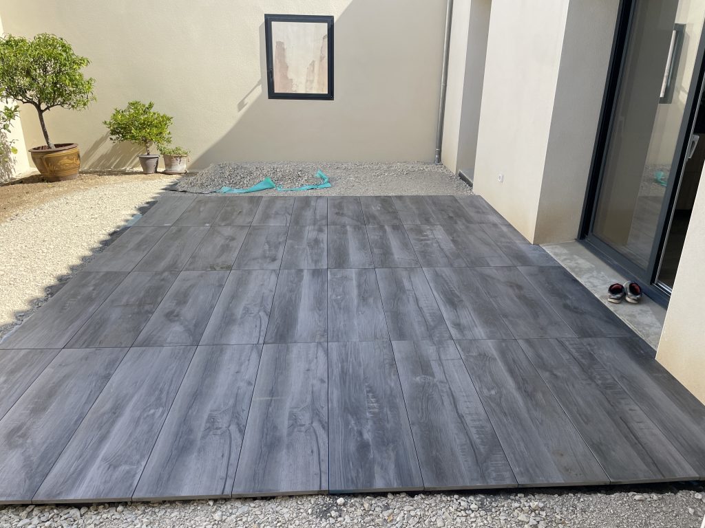 Pose de dalles en grès cérame gris sur terrasse extérieure, finition moderne et résistante le long d’un mur de façade.
