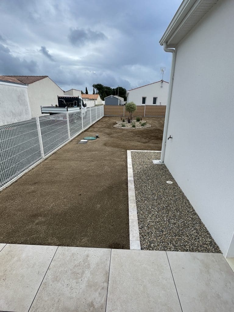 Préparation de sol le long d’une clôture avec bordures et zones gravillonnées, base prête pour engazonnement ou aménagement paysager.
