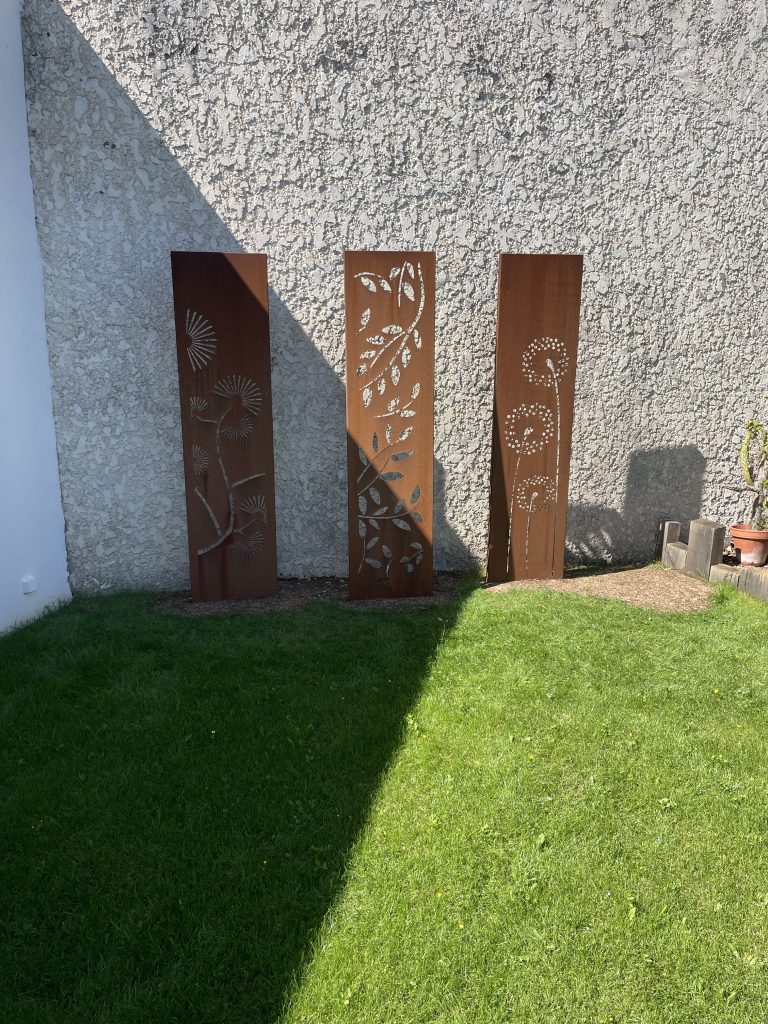 Panneaux décoratifs en acier corten installés dans un jardin, créant une séparation esthétique entre pelouse et mur extérieur.