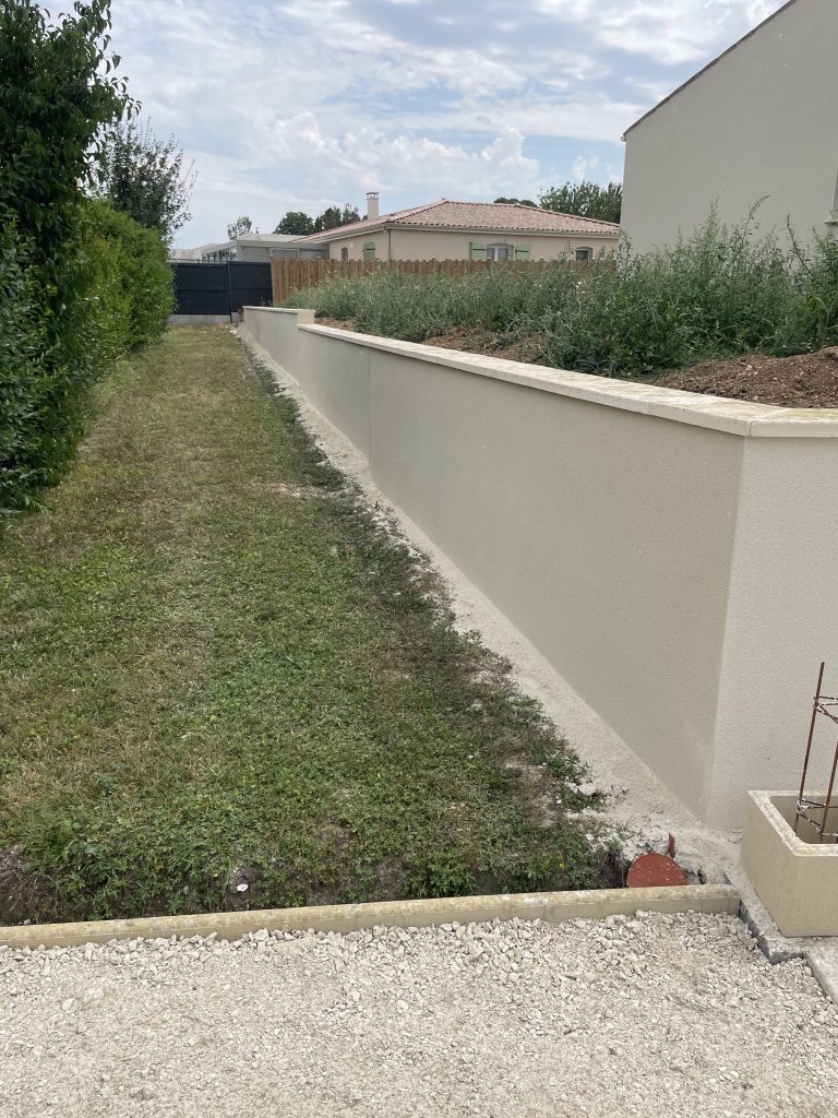 Allée engazonnée bordée d’un muret enduit et de haies, aménagement paysager simple et fonctionnel pour passage piéton.