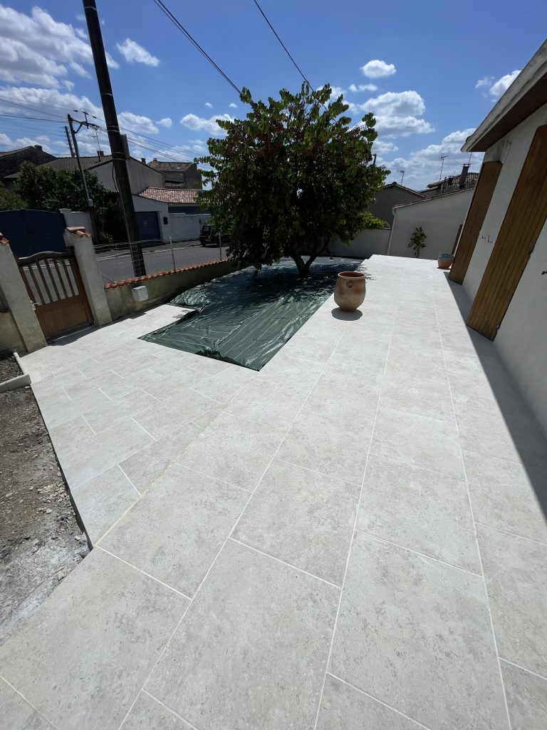 Grande terrasse en dalles claires avec zone protégée et aménagement paysager, espace extérieur lumineux et durable.