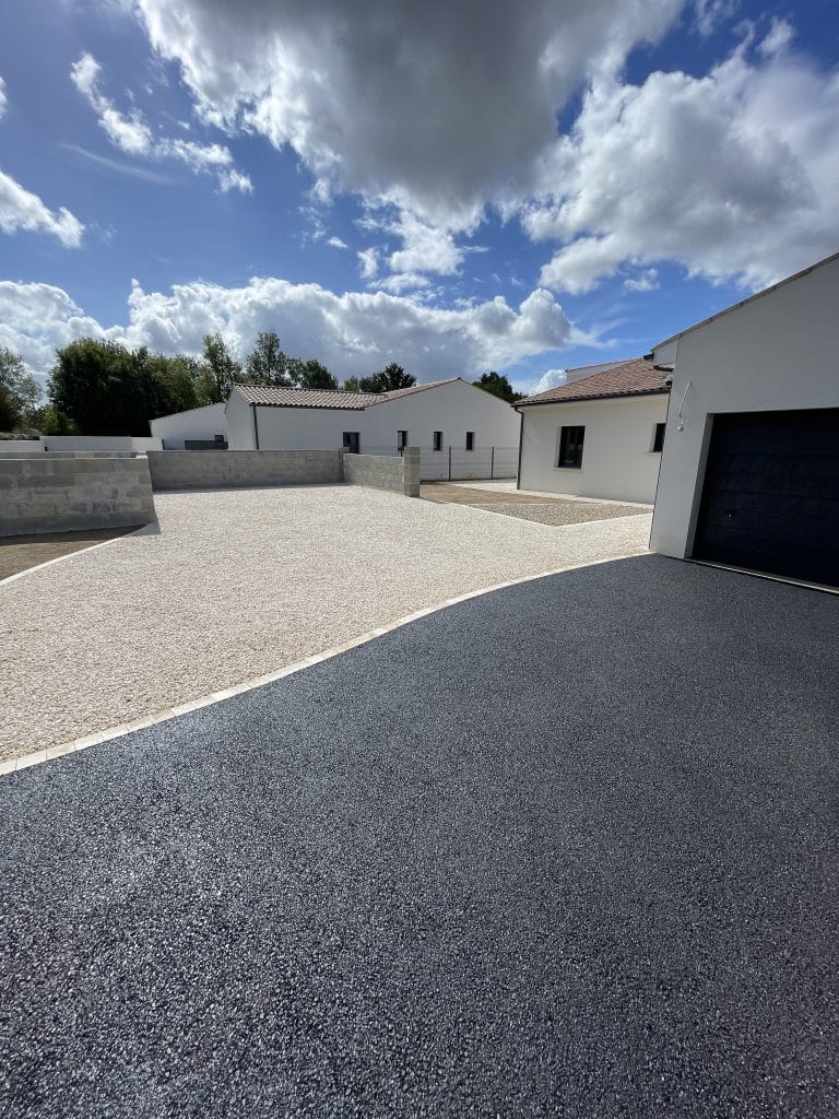 Grande allée mixte en enrobé et gravier clair devant une maison contemporaine, avec mur de soutènement et accès véhicules.